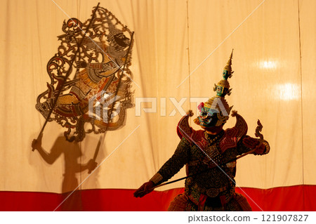 Low light shot of man as giant charactor with Khon or Mask dance costume stand with performance action in front of grand shadow play Low light shot of man as giant charactor with Khon or Mask dance costume stand with performance action in front of grand shadow play 121907827