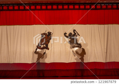 Wide shot of two shadow of grand shadow play with the player hold crafts and stand behide the screen. Wide shot of two shadow of grand shadow play with the player hold crafts and stand behide the screen. 121907879