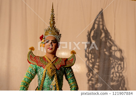 One man with Khon or Mask dance dress stand with performance action in front of grand shadow play in the background with white screen. One man with Khon or Mask dance dress stand with performance action in front of grand shadow play in the background with white screen. 121907884