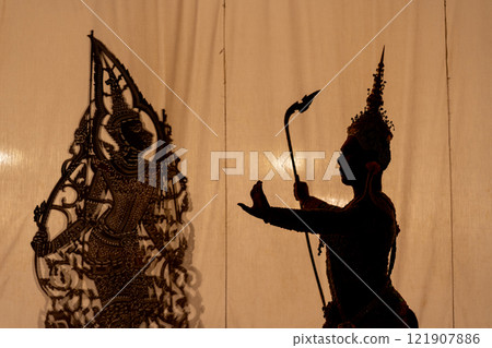 Silhouette of Khon or Mask dance player stand with performance action in front of grand shadow play in the background with white screen. Silhouette of Khon or Mask dance player stand with performance action in front of grand shadow play in the background with white screen. 121907886