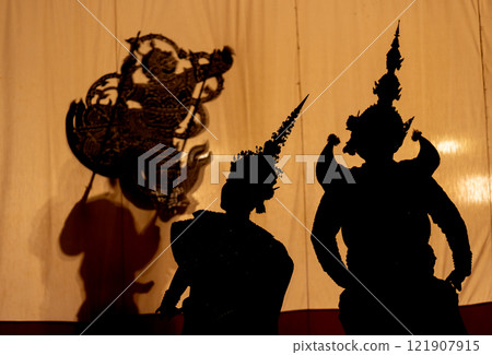 silhouette of man as giant charactor and woman with Khon or Mask dance costume stand with performance action in front of grand shadow play in the background with white screen. 121907915