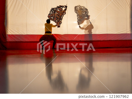 The player men stand with perform grand shadow play with one stand in front of white screen with reflection on the floor. 121907962