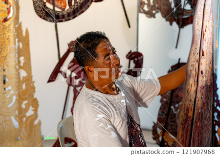 Side view and close up Asian senior man hold the piece of grand shadow play craft and look with happiness also stay in area of workplace and he also pround for his work. 121907968