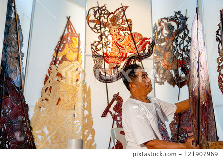 Asian senior man hold the piece of grand shadow play craft and look with happiness also stay in area of workplace and he also pround for his work. 121907969