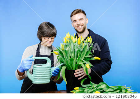 Flower shop. A young guy helps an older woman florist take care of flowers in a flower studio 121908046
