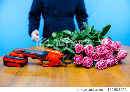 Man in apron cuts off the ends of a rose on blue background 121908051