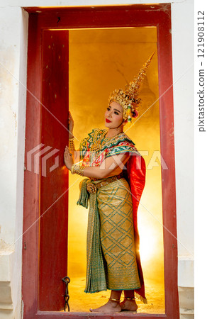 Vertical and wide shot image of woman with Khon mask charactor as angel stand in front of door frame of old building and look to her right side with warm light in the background. Vertical and wide shot image of woman with Khon mask charactor as angel stand in front of door frame of old building and look to her right side with warm light in the background. 121908112