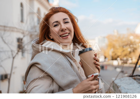 Woman Coffee Autumn City: Smiling mature woman enjoys coffee outdoors during autumn in a city. 121908126