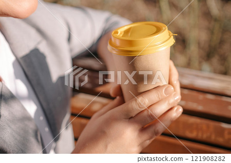 A person holding a coffee cup with a yellow lid. The person is wearing a gray jacket and white shirt. A person holding a coffee cup with a yellow lid. The person is wearing a gray jacket and white shirt. 121908282