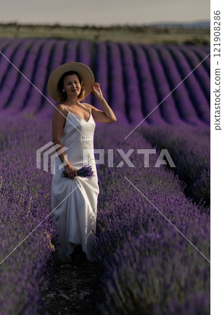 A woman in a white dress is walking through a field of purple flowers 121908286