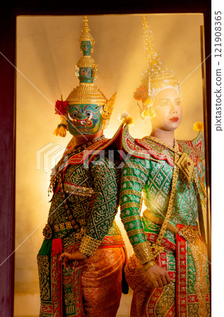 Vertical image of two charactors of Khon mask costume stand with backs leaning against each other at door frame with beam light in the back. Vertical image of two charactors of Khon mask costume stand with backs leaning against each other at door frame with beam light in the back. 121908365