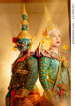 Vertical image and close up of two charactor of Khon mask costume stand with backs leaning against each other at door frame with beam light in the back. 121908367