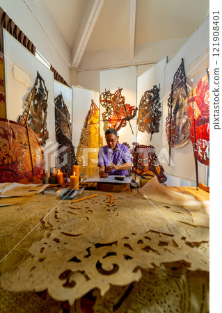 Vertical image Asian senior man wear glasses use hammer and chisel to create grand shadow play craft and he concentrate to work in area of workplace with several products are place around workplace. Vertical image Asian senior man wear glasses use hammer and chisel to create grand shadow play craft and he concentrate to work in area of workplace with several products are place around workplace. 121908401