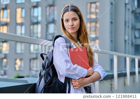 Portrait of young smiling college student girl with backpack textbook, outdoors 121908411