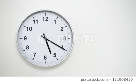 Minimalist White Clock with Silver Frame Striking 17.20/05.20 on White Background. Perfect for Time Management and Corporate Campaigns 121908430