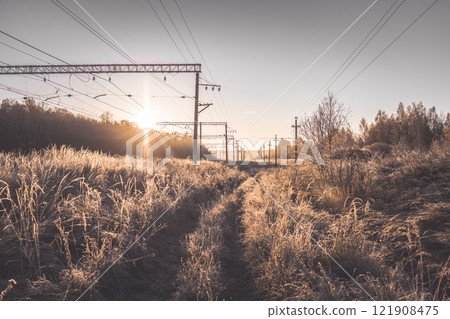 Suburban morning winter landscape of a railway station. The sun fills dry bushes and grass with soft golden light. Winter landscape of nature covered with frost Suburban morning winter landscape of a railway station. The sun fills dry bushes and grass with soft golden light. Winter landscape of nature covered with frost 121908475