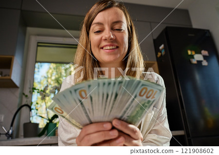 Smiling woman in kitchen counting cash while sitting at table with receipts and documents, managing home finances. Concept of planning home budget Smiling woman in kitchen counting cash while sitting at table with receipts and documents, managing home finances. Concept of planning home budget 121908602