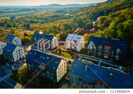 Modern residential buildings near vibrant autumn forest, aerial view. Contemporary apartments in suburban eco friendly neighborhood with green spaces near mountains in small European town 121908604