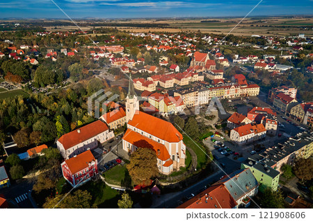 Aerial view of European town with colorful buildings and church at sunset. Suburban landscape with red roofed houses in small city surrounded by lush greenery and countryside fields Aerial view of European town with colorful buildings and church at sunset. Suburban landscape with red roofed houses in small city surrounded by lush greenery and countryside fields 121908606