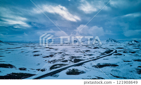 A road in a snowy landscape with mountains towering in the distance 121908649