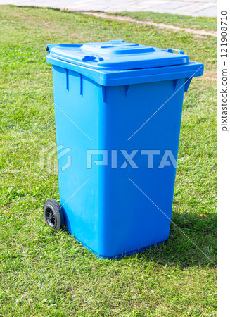 Covered blue plastic garbage container with wheels on the green grass 121908710