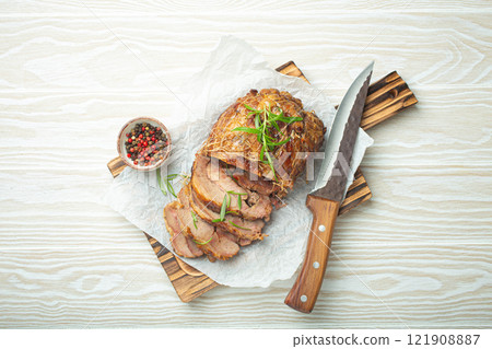 Rolled turkey roasted with spices and herbs on baking paper with knife and wooden white background top view. Baked cut for slices turkey fillet roll for dinner 121908887