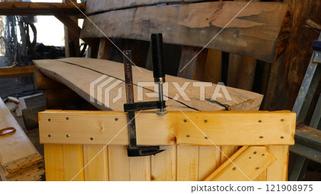 using a clamp to glue a chip to a chip in a wooden barn door in a carpenter's workshop, repairing a plank door panel using a clamp, pulling and gluing together plank door parts using a clamp to glue a chip to a chip in a wooden barn door in a carpenter's workshop, repairing a plank door panel using a clamp, pulling and gluing together plank door parts 121908975