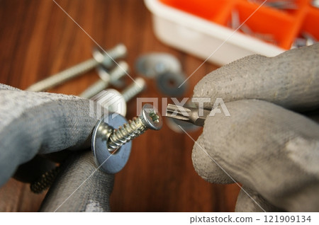 Screw and screwdriver bit in builder's hands. Close-up of the builder's work process. 121909134