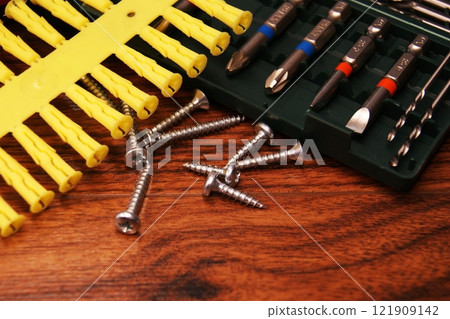 Screws, plastic dowels and a set of bits on a wooden table Screws, plastic dowels and a set of bits on a wooden table 121909142