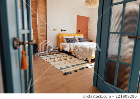 A cozy bedroom with white walls. An open stylish blue door. Wooden bed with stylish bedside tables and a soft fluffy carpet. Modern and comfortable interior. 121909290