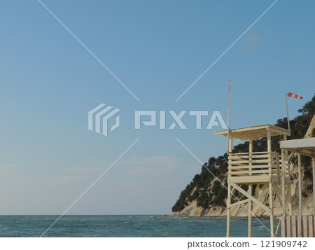 empty wooden lifeguard lookout tower on rocky beach on sunny windy day, deserted sea coast landscape with wooden structure for shore view empty wooden lifeguard lookout tower on rocky beach on sunny windy day, deserted sea coast landscape with wooden structure for shore view 121909742