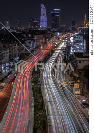 Nightscape view with bright glowing light trails of many cars on the road of Bangkok with Skyscrapers in the background. 121910144