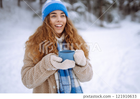 Smiling woman with a thermos in a snowy forest enjoying nature. Adventure concept. Lifestyle. 121910633