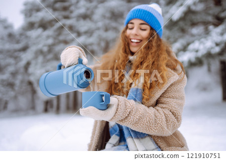 Smiling woman with a thermos in a snowy forest enjoying nature. Adventure concept. Lifestyle. 121910751