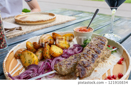 Georgian lula kebab with baked potatoes, sauce and greens. Grilled souvlaki, minced meat kebap, lamb on skewers Georgian lula kebab with baked potatoes, sauce and greens. Grilled souvlaki, minced meat kebap, lamb on skewers 121910834