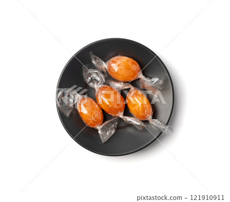 Orange hard candies on black plate isolated. Lollipop pile, wrappers fruit confectionery group 121910911