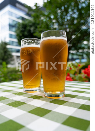 Two beer glasses at outdoor cafe, cold pint glass on checkered tablecloth table, cool condensation Two beer glasses at outdoor cafe, cold pint glass on checkered tablecloth table, cool condensation 121911543