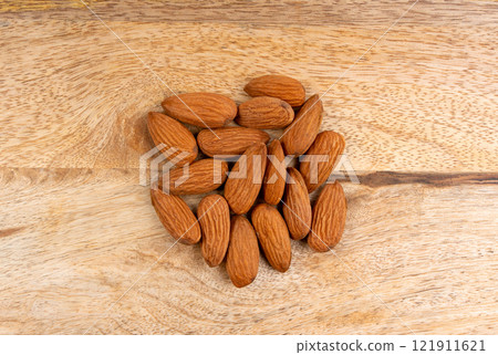 Almonds pile, nut group, whole almond seeds, brown scattered fruit kernels, dry raw nuts on wood Almonds pile, nut group, whole almond seeds, brown scattered fruit kernels, dry raw nuts on wood 121911621