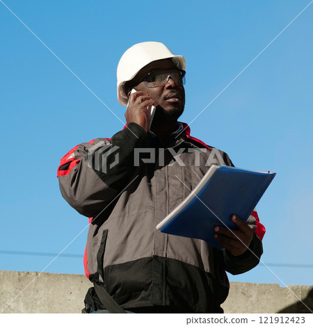 African american builder with work papers talks on smartphone African american builder with work papers talks on smartphone 121912423