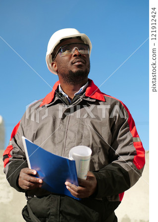 African american worker stands at construction site with work papers African american worker stands at construction site with work papers 121912424