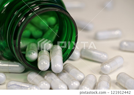 Capsules with blue powder and open green container lies on the white table Capsules with blue powder and open green container lies on the white table 121912442