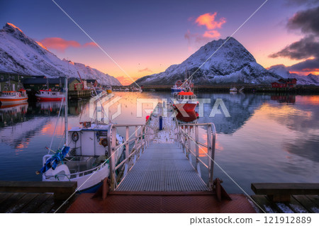 Red fishing boats on the sea, snowy mountains at colorful sunset 121912889