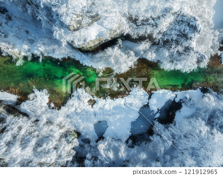 Aerial view of a vibrant emerald green river and snowy trees 121912965