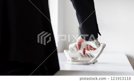 Businessman dialing telephone number on a classical white landline telephone Businessman dialing telephone number on a classical white landline telephone 121913118
