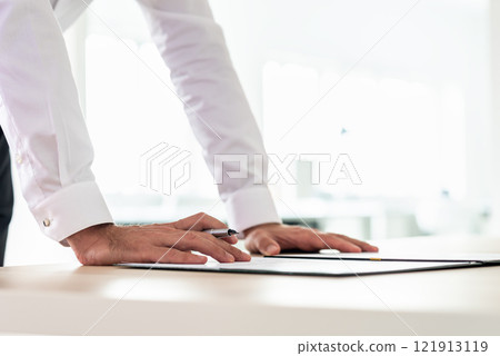 Businessman leaning on office desk to sign a document Businessman leaning on office desk to sign a document 121913119