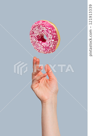 Hand with levitation glazed pink donut on blue background. Hand with levitation glazed pink donut on blue background. 121913339