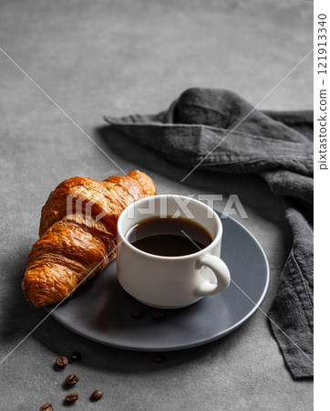 Cup of espresso coffee and fresh croissant on grey plate on dark background with napkin Cup of espresso coffee and fresh croissant on grey plate on dark background with napkin 121913340