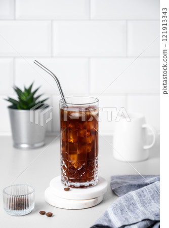 Cold brew coffee in a glass with ice and straw on a light table against a white brick background 121913343