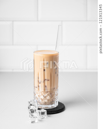Cold latte coffee in a tall glass with milk and straw on a light table on a white brick background Cold latte coffee in a tall glass with milk and straw on a light table on a white brick background 121913345
