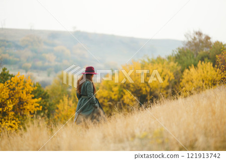 Beautiful stylish girl walks in the autumn park. The girl is dressed in a green coat and a red hat. 121913742